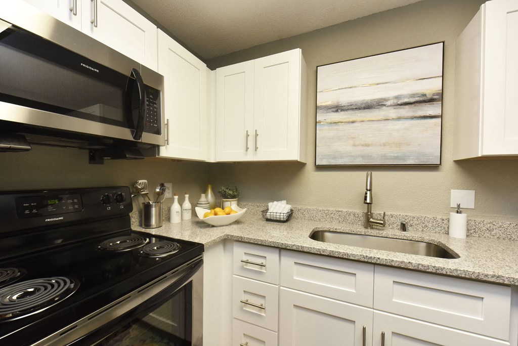 a kitchen with a stove sink and microwave and white cabinets