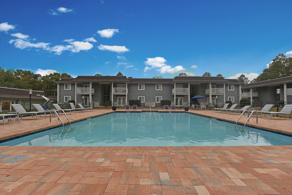 Apartments Near Region Field - MarQ Vestavia - Pool With Grey Sun Lounge Chairs, Brick-Style Flooring, Blue Sun Umbrella, And View Of Apartment Complex