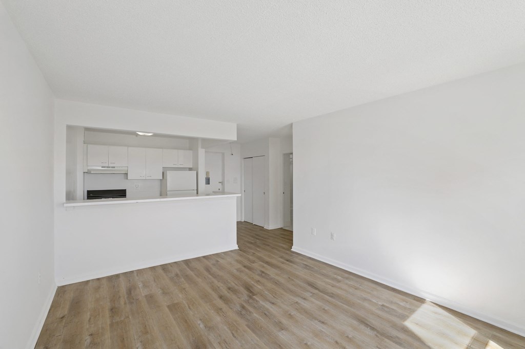 the living room and kitchen of an apartment with white walls and wood flooring