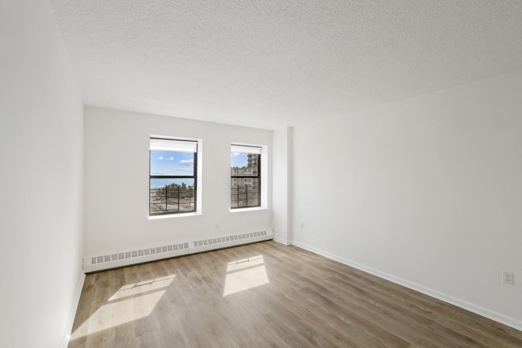 the living room of an empty apartment with wood flooring and two windows