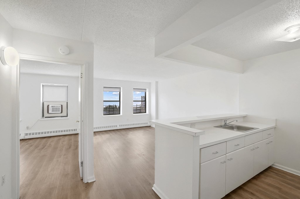 the living room and kitchen of an apartment with white cabinets and wood flooring
