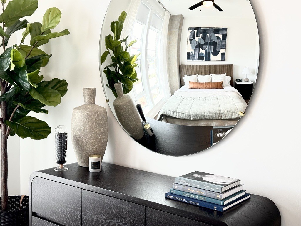 A round mirror reflects a bedroom with a bed and a nightstand.