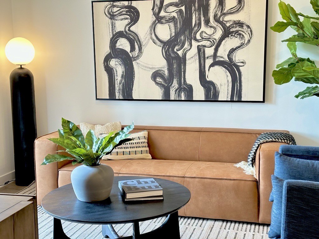 A living room with a couch, a table, a lamp, and a painting on the wall.