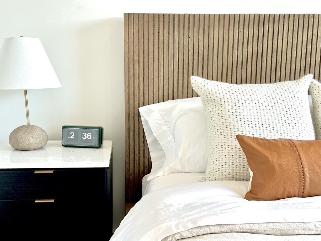 A bed with white pillows and a lamp on a nightstand.