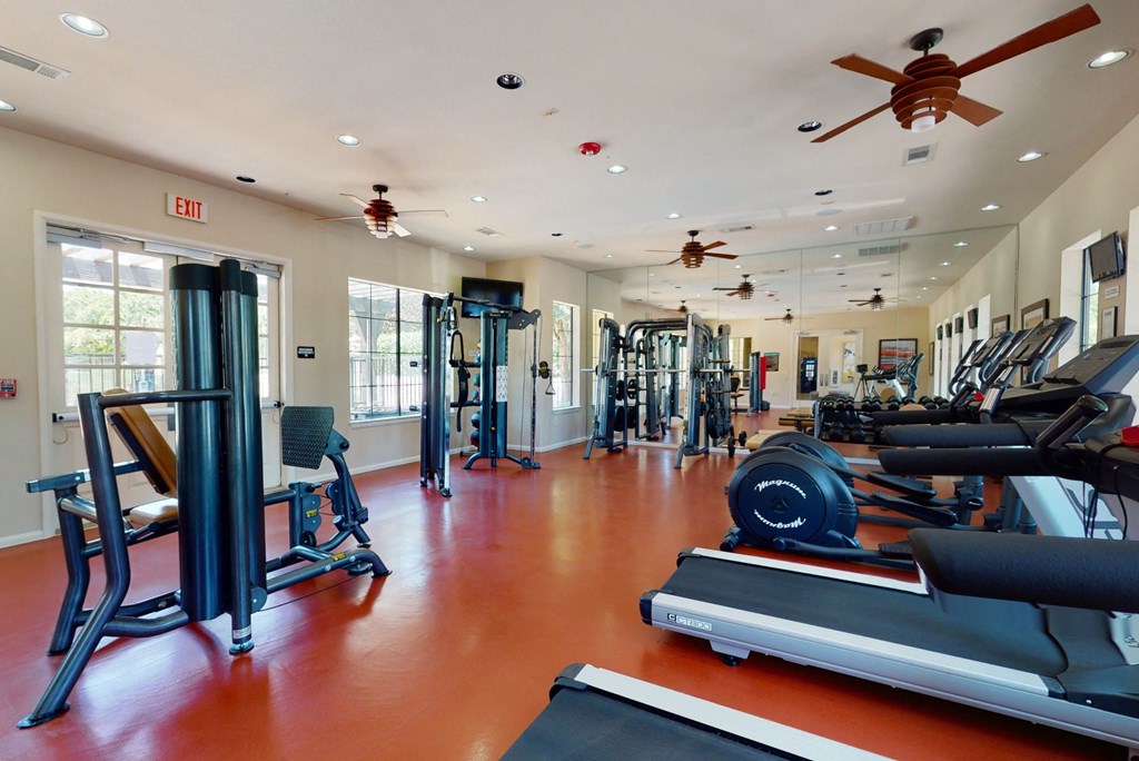 a gym with cardio equipment and ceiling fans