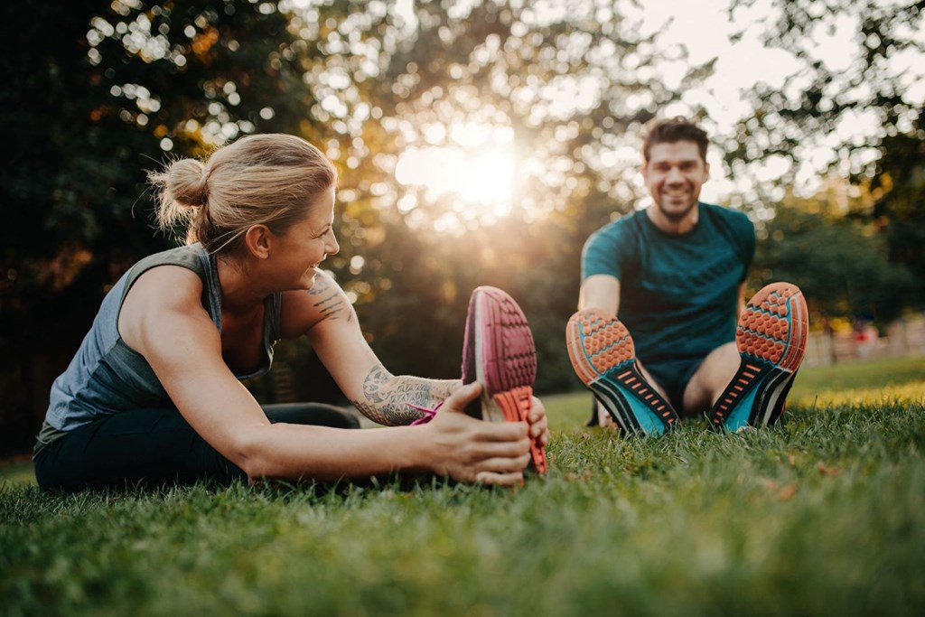 a man and woman sitting on the grass touching their shoes