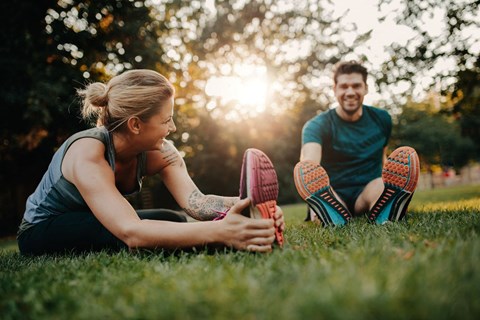 a man and woman sitting on the grass touching their shoes