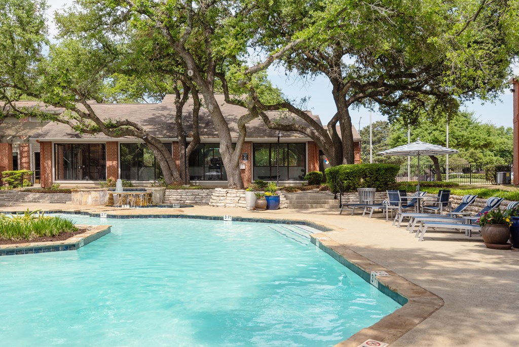 a pool with lounge chairs and umbrellas in front of a house with a thatched
