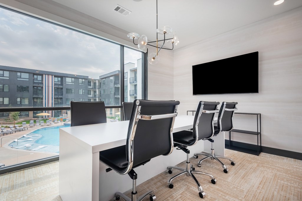 A room with a white desk and black chairs with a large window overlooking a pool.
