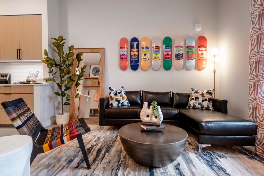 A living room with a black leather couch, a wooden chair, a coffee table, and a wall with skateboards on it.