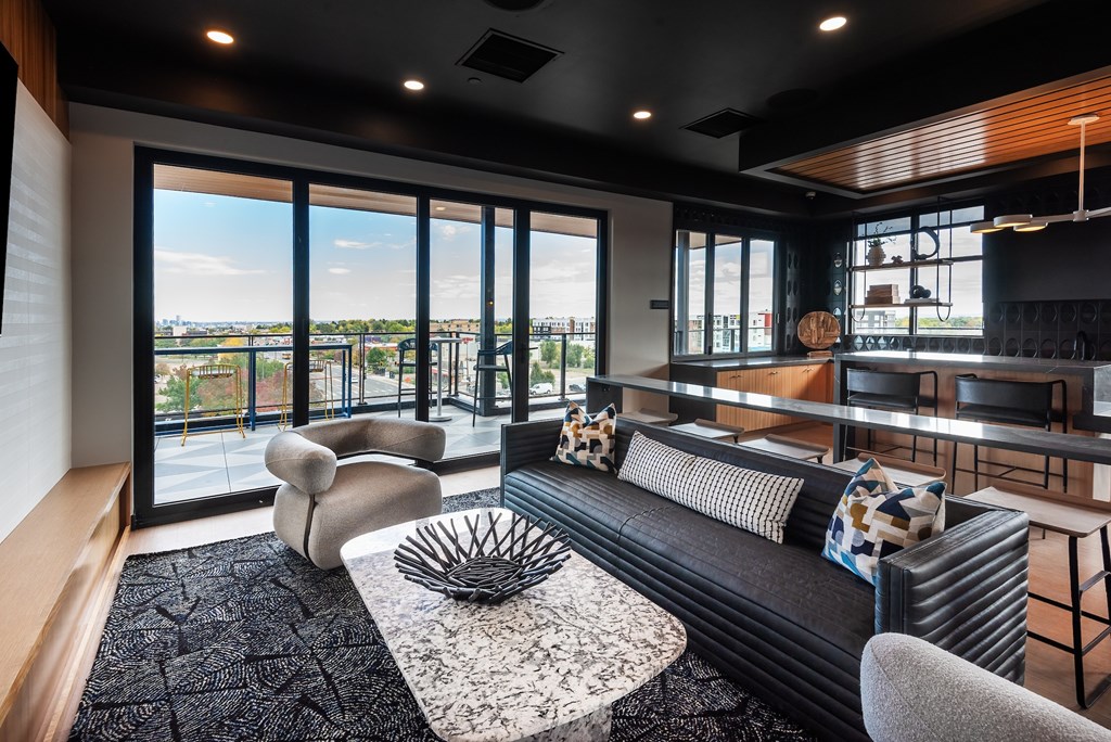 A black couch with a white pillow is in the middle of a room with a large window.