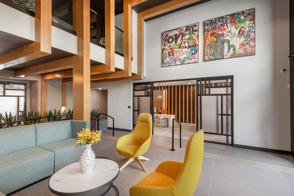 A modern living room with a blue sofa, yellow chairs, and a white vase with yellow flowers on a round table.
