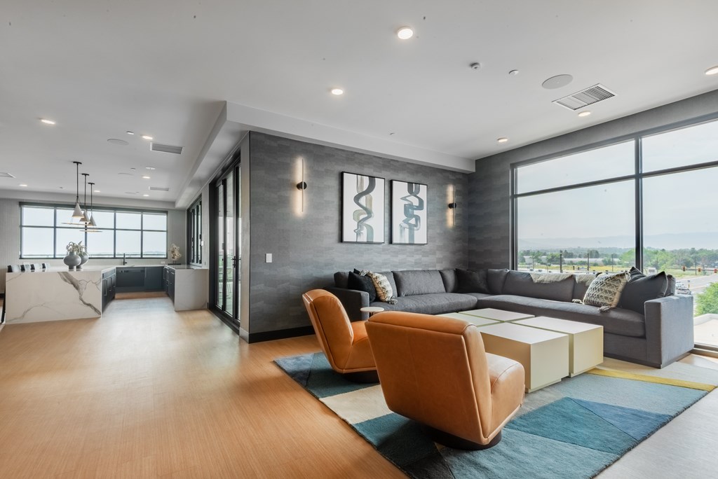 A modern living room with a grey couch, a wooden floor, and a large window.