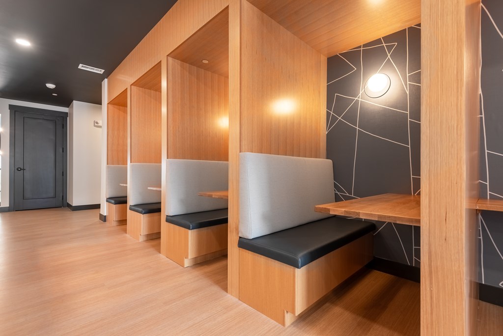 A row of wooden benches with black cushions are lined up in a room.