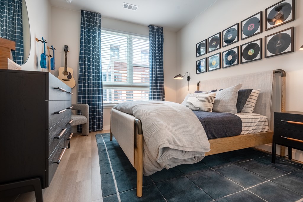 A bedroom with a bed, a chair, a dresser, and a window with curtains.