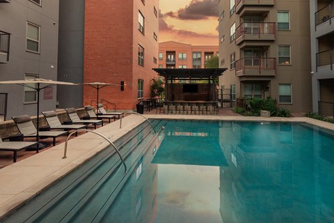 an apartment pool with a sunset in the background at The Can Plant Residences at Pearl, San Antonio, Texas
