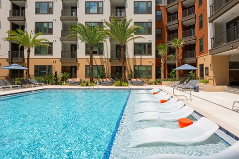 A swimming pool with lounge chairs and palm trees in front of a multi-story apartment building.