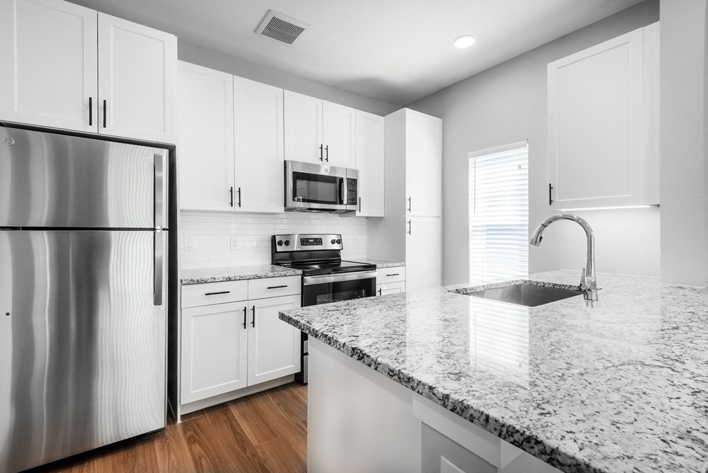 a kitchen with white cabinets and granite counter tops and a stainless steel refrigerator
