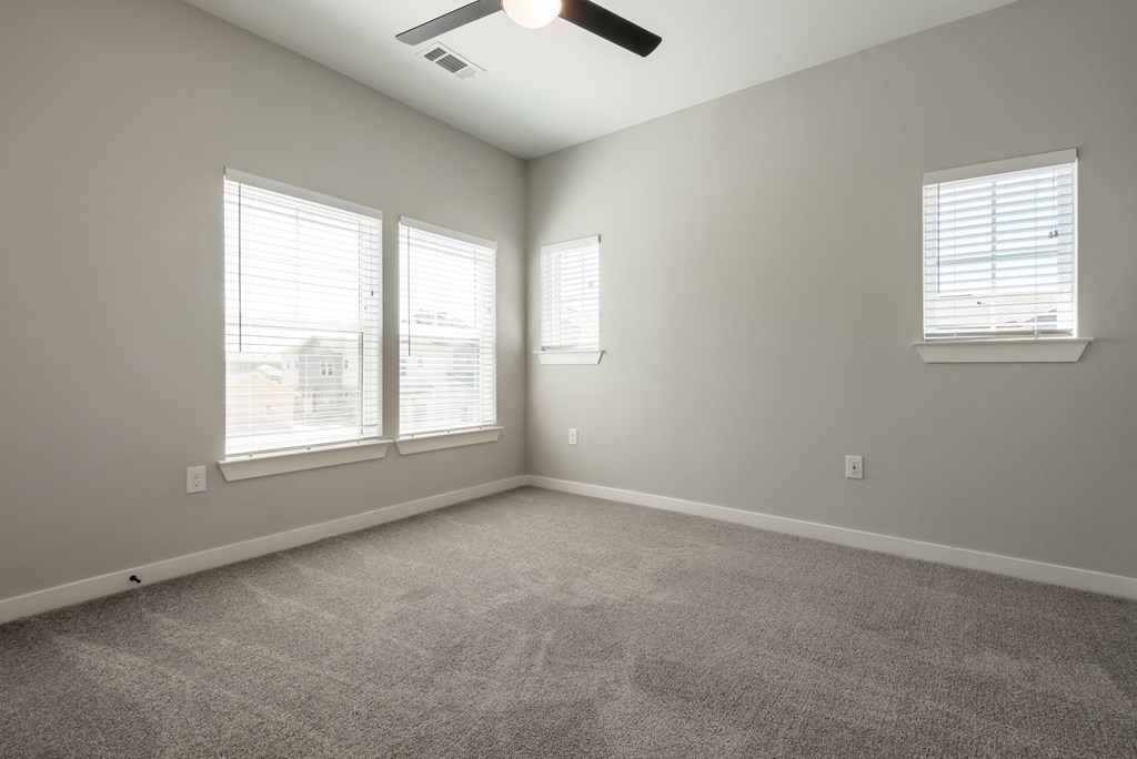 an empty living room with three windows and a ceiling fan