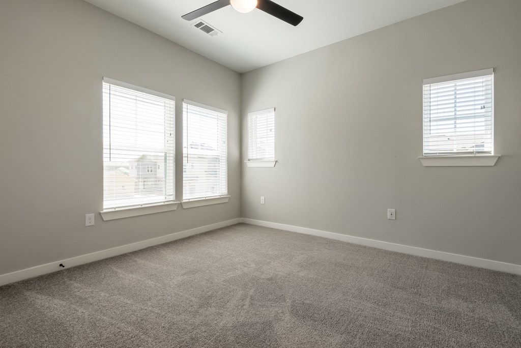 an empty living room with three windows and a ceiling fan