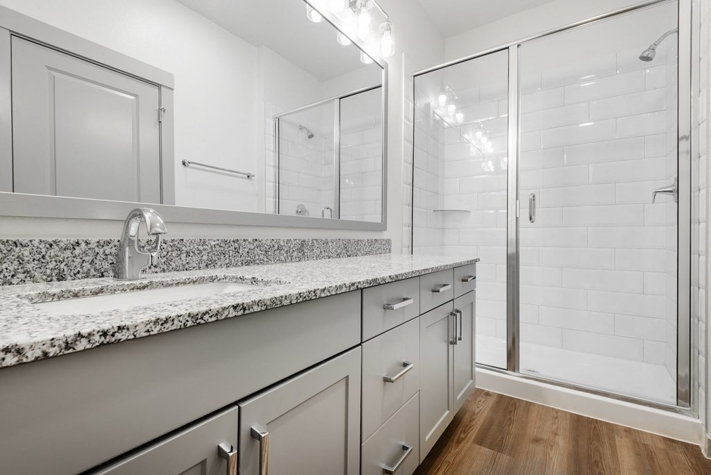 a bathroom with white cabinets and granite counter tops and a shower