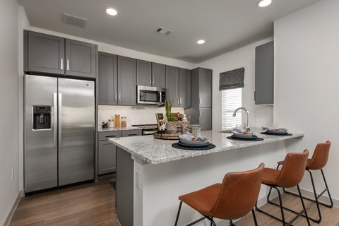 A modern kitchen with a refrigerator, microwave, and a counter with chairs.