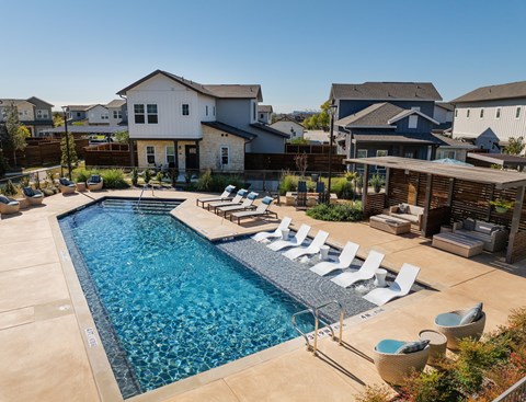 A swimming pool surrounded by lounge chairs and a wooden pergola.