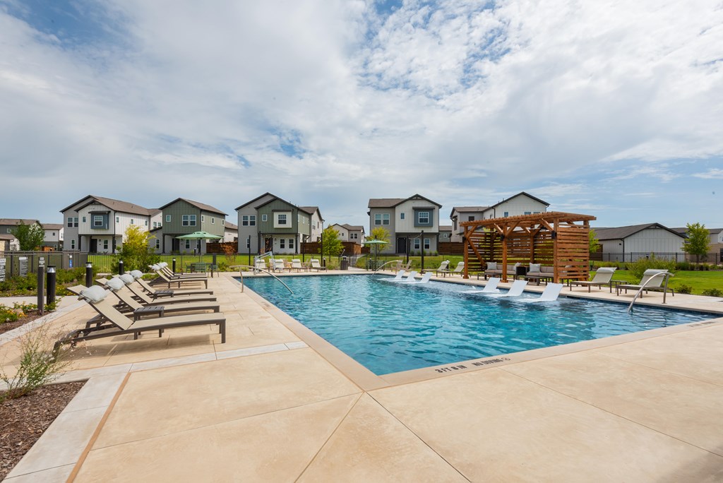 A swimming pool surrounded by lounge chairs and a wooden pergola.