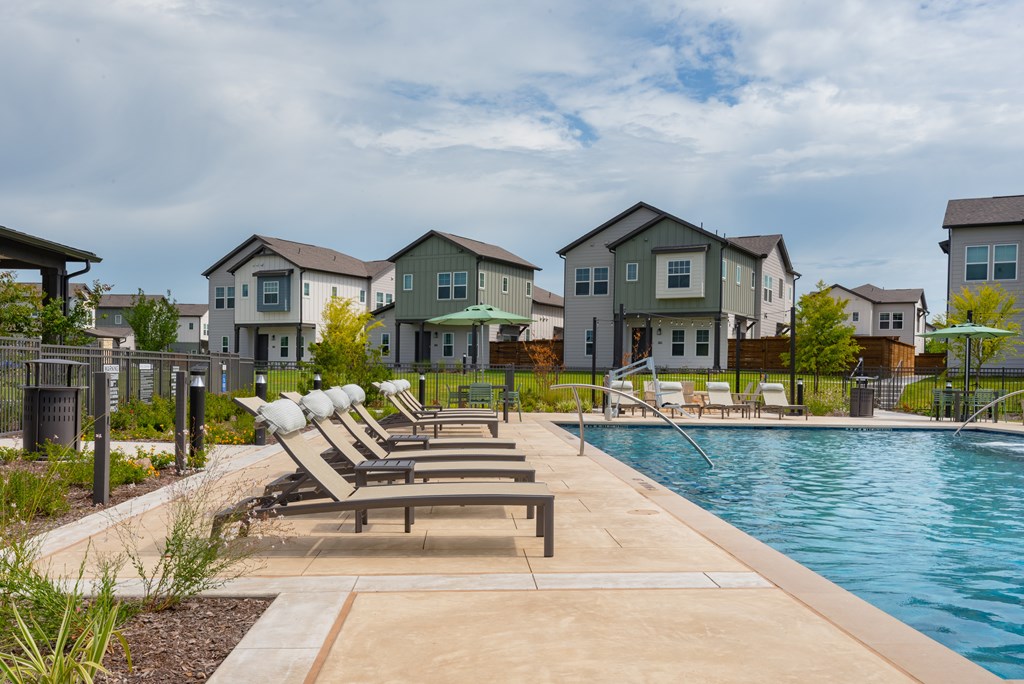 A pool with lounge chairs and apartment buildings in the background.