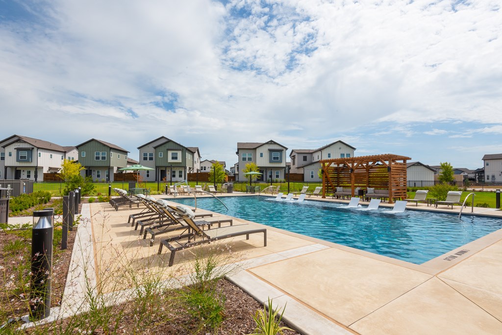 A swimming pool surrounded by lounge chairs and a row of houses in the background.