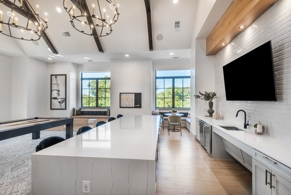 A modern kitchen with a pool table and a view of trees outside the window.