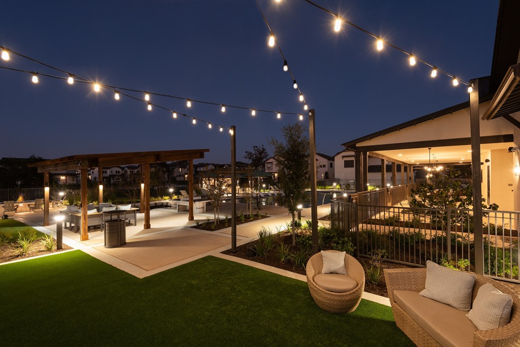 A patio area with a lawn, a hanging chair, and a couch under string lights.
