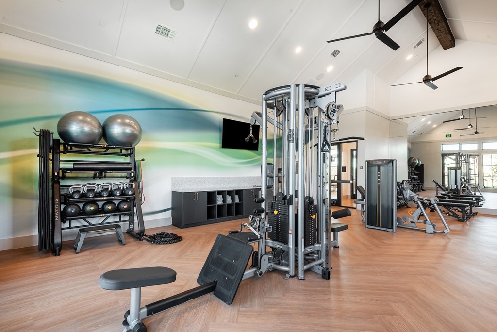 A gym with a variety of equipment including a bench, weights, and a television.