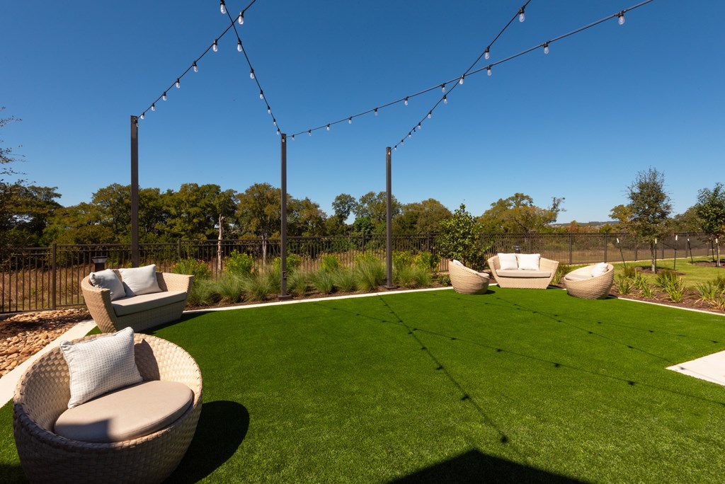 A backyard with a lawn, chairs, and string lights.
