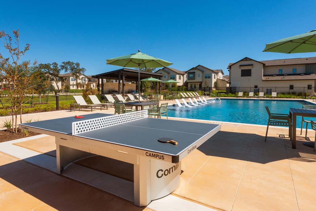 A ping pong table is in the middle of a pool and is surrounded by chairs.