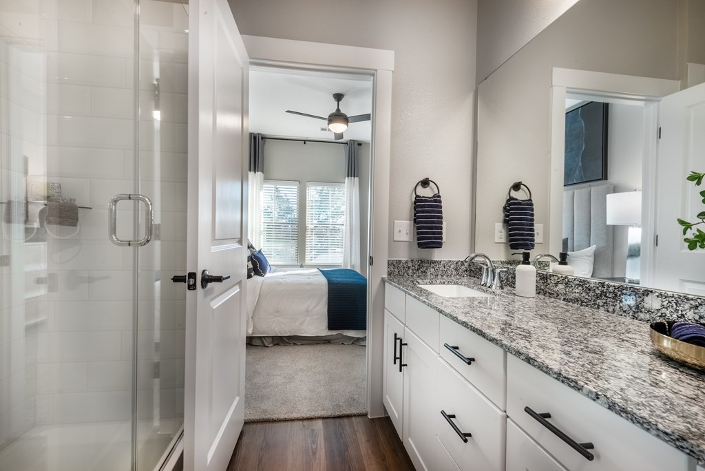A bathroom with a walk-in shower, a bed, and a vanity with a mirror.