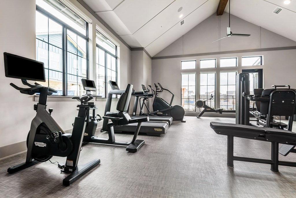 a gym with cardio equipment and weights in a building with large windows