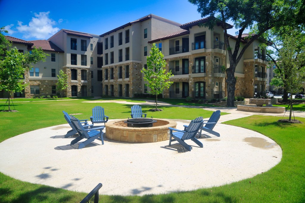 an outdoor firepit with adirondack chairs in front of an apartment building