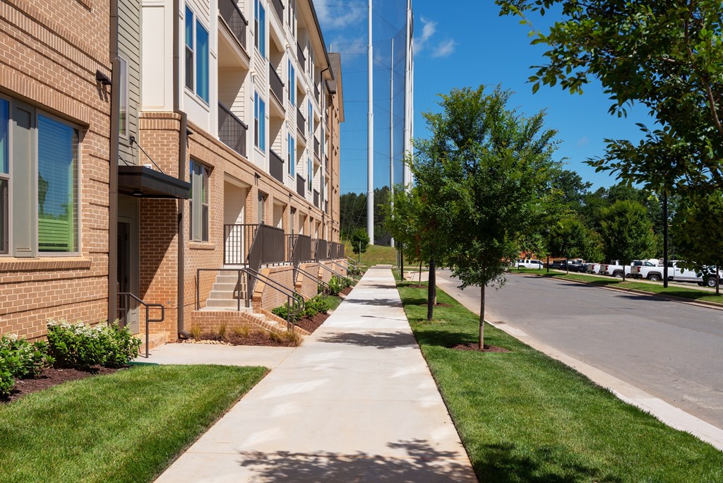 A long concrete walkway leads the eye through a grassy area to a building.