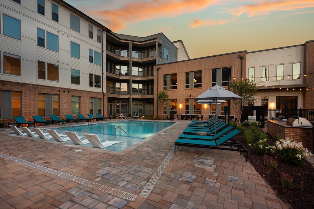 A swimming pool surrounded by lounge chairs and umbrellas in front of a building.