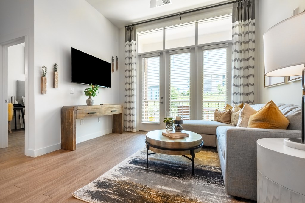 A living room with a grey couch, a wooden table, and a flat screen TV mounted on the wall.