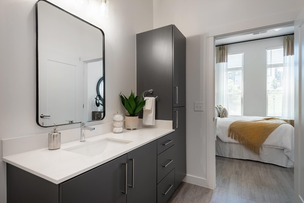 A bathroom with a sink, mirror, and a bedroom in the background.