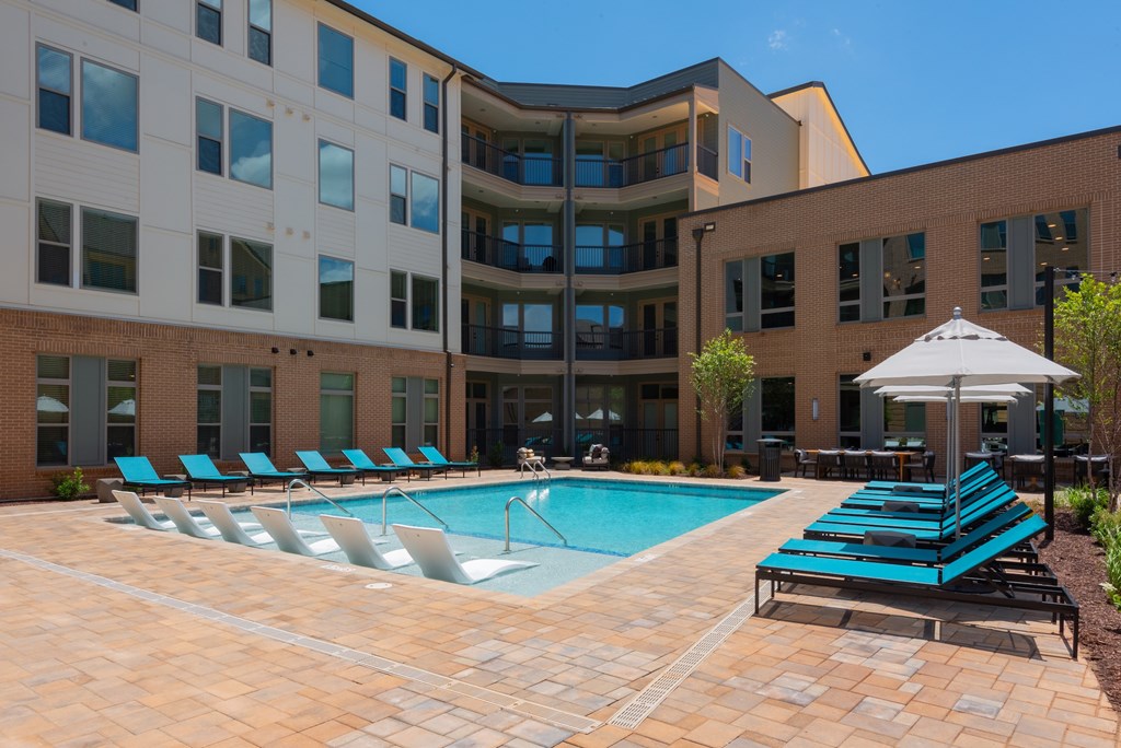 A pool area with sun loungers and a building in the background.