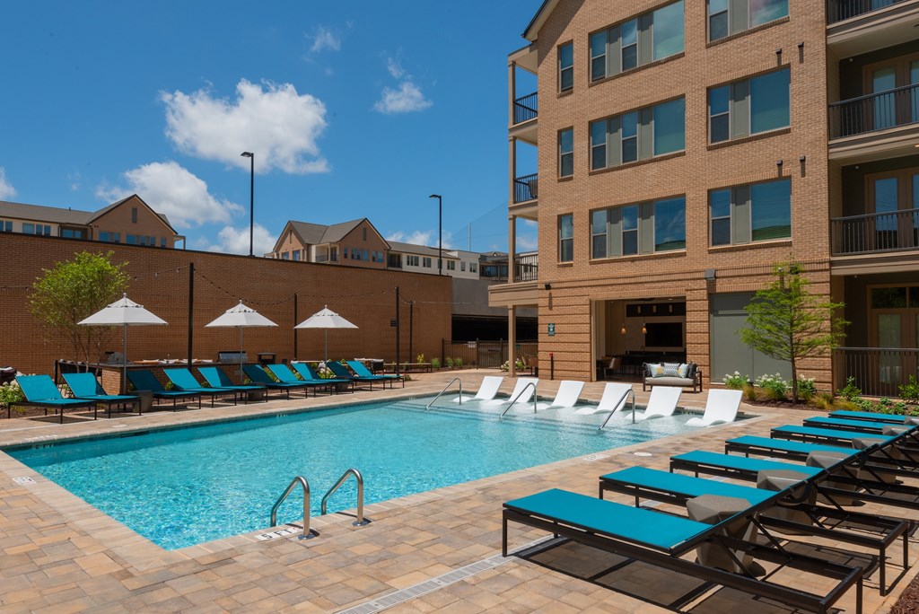 A pool with lounge chairs and umbrellas in front of a building.