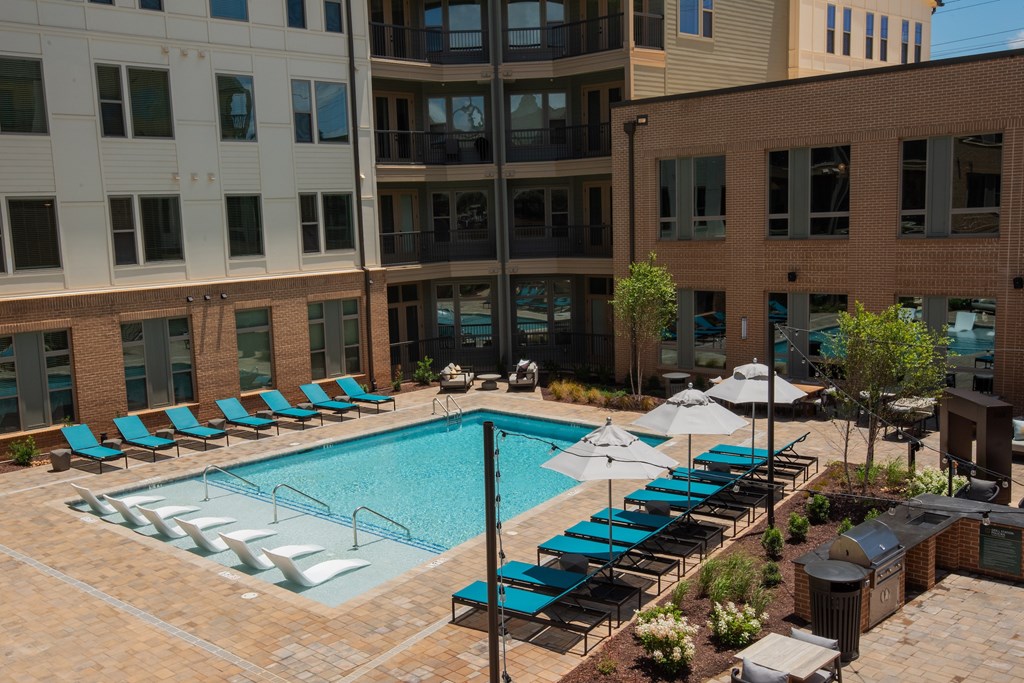 A pool surrounded by chairs and umbrellas with buildings in the background.