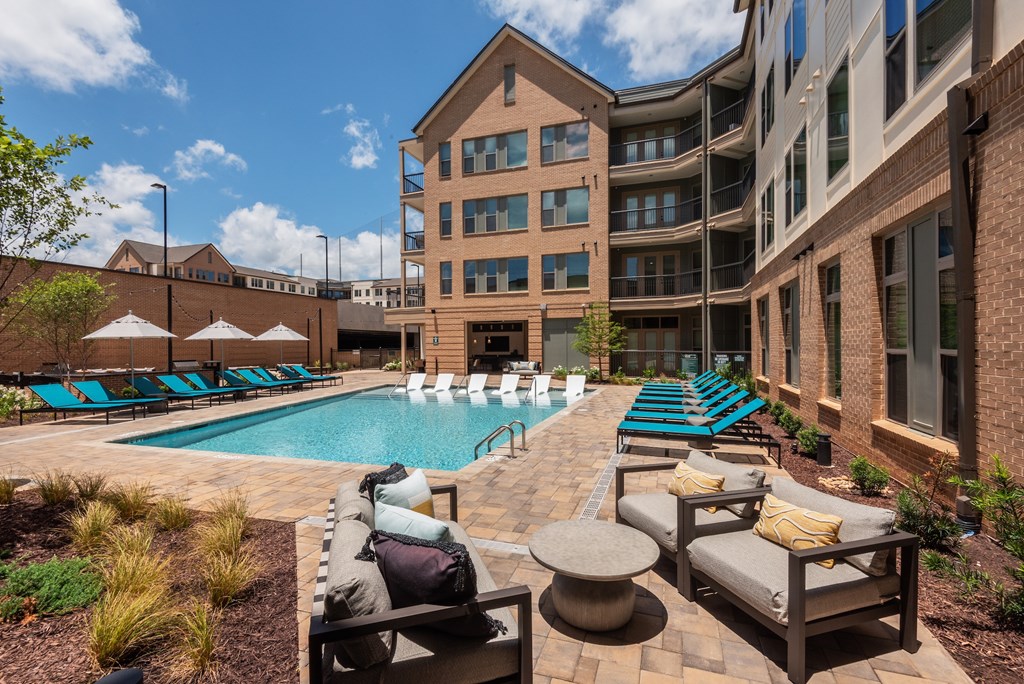 A pool surrounded by chairs and umbrellas in front of a building.