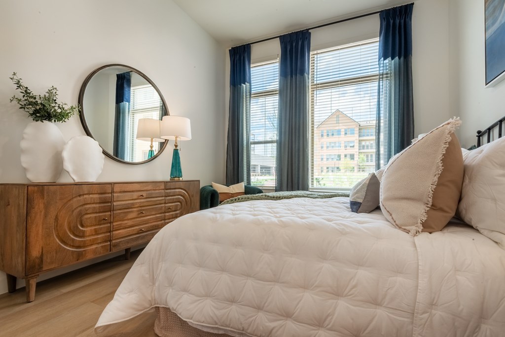 A bedroom with a large bed, a wooden dresser, and a round mirror on the wall.