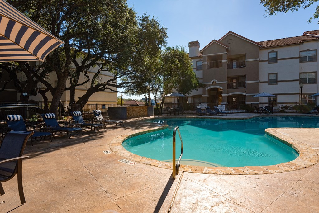 a swimming pool with chairs and an umbrella in front of an apartment building  at Hayden on West Ave, San Antonio, TX, 78216