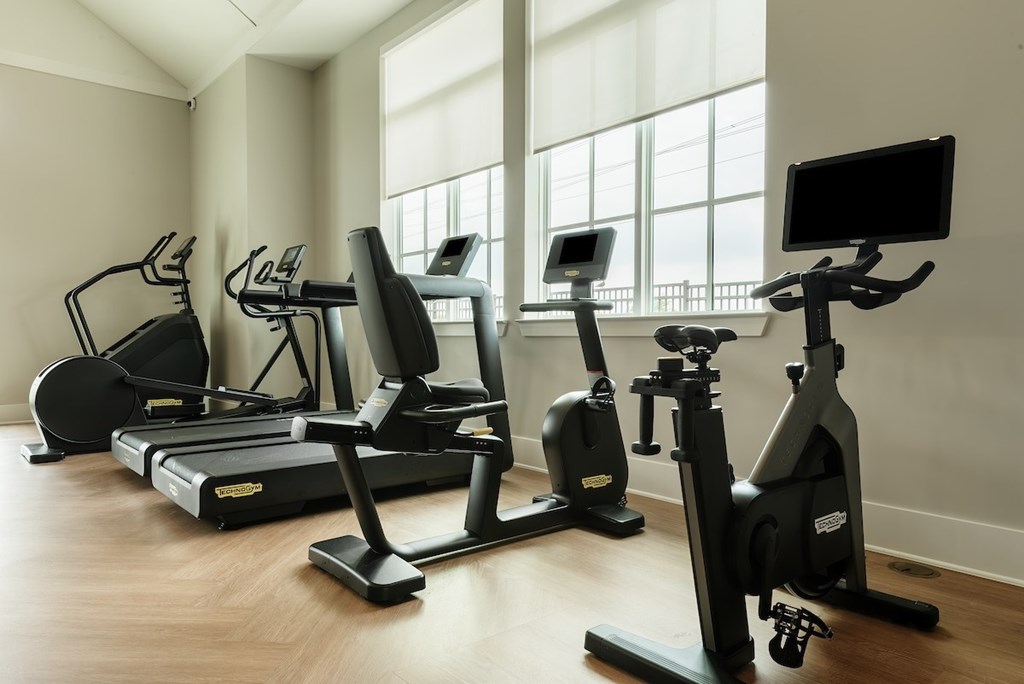 A row of treadmills, stationary bikes, and elliptical machines are lined up in a row in a brightly lit room.
