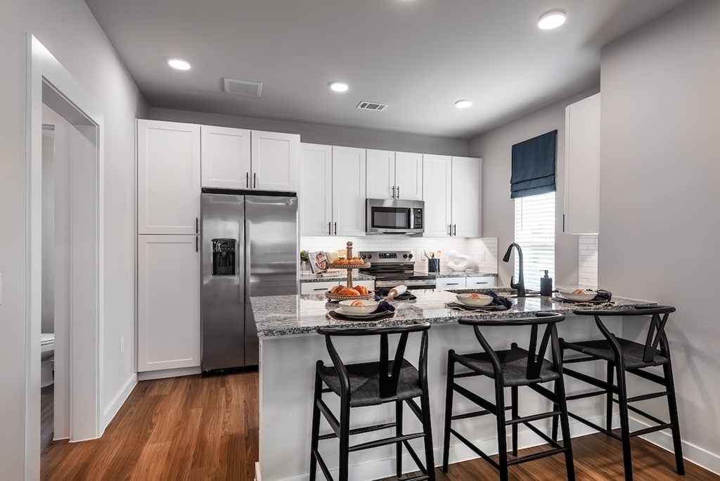 A kitchen with a refrigerator, microwave, and a counter with a table and chairs.